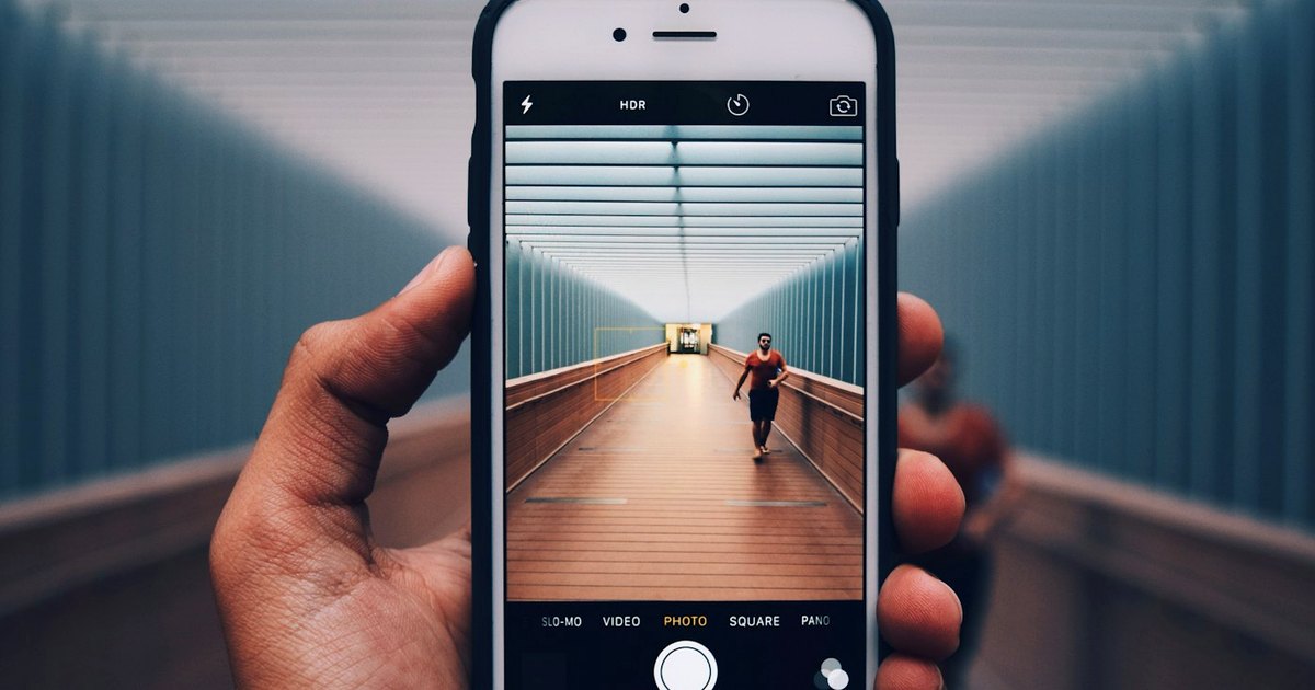 Hand holding a smartphone, taking a photo of a person walking along a covered footbridge